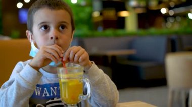 Kafede maske takan küçük bir çocuk kek yiyor. Salgın sırasında kafede maske takan bir çocuk.