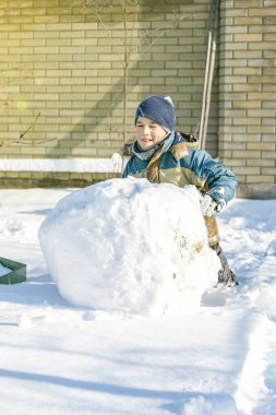 Çocuk, açık kış gününde evin arka bahçesinde bir kardan adam heykeli yaptı. Oğlan yoğun bir kar yağışı sırasında bahçede bir kardan adam yapmak için bir kartopu yuvarlar. ses tonlu.