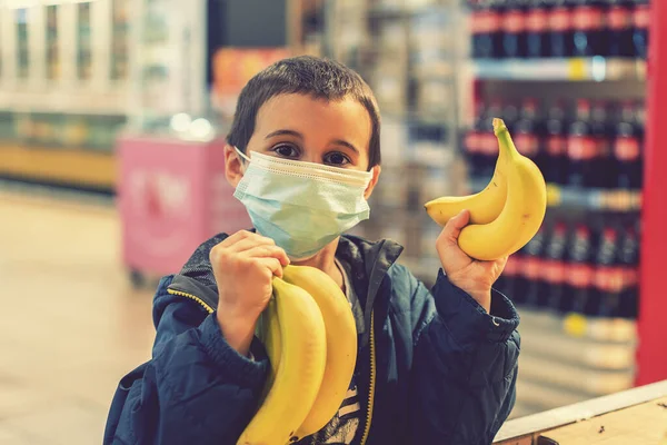 Child wearing surgical face mask buying fruit in supermarket in coronavirus pandemic. little boy in a supermarket is wearing a medical mask. Coronavirus quarantine. toned