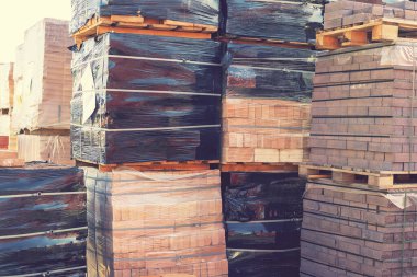 Açık havada kırmızı tuğlalı paletler. İnşaat malzemeleri toptan satılıyor. Sokaktaki bir inşaat deposunda yeni üretilen kırmızı tuğla paketleri. Onarım ve inşaat malzemeleri kavramı