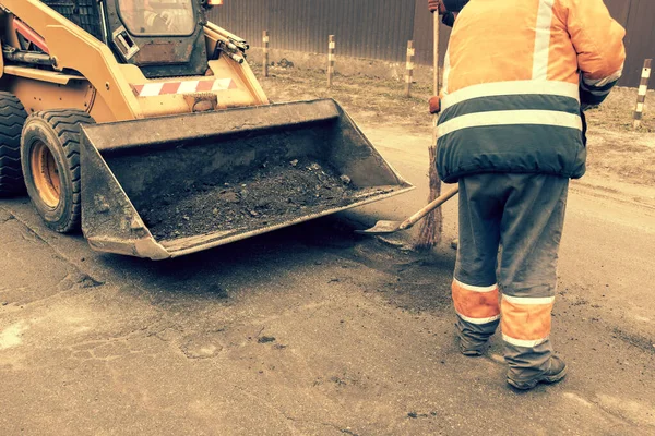 Los trabajadores del camino en uniformes reflectantes naranja brillante utilizan palas para raspar la arena acumulada. mantenimiento de pavimentos de carreteras y carreteras. trabajos de reparación de baches. tonificado. — Foto de Stock