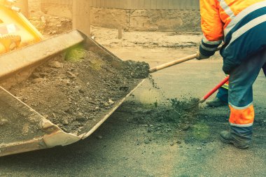 Parlak turuncu yansıtıcı üniformalı yol işçileri birikmiş kumu kazmak için kürek kullanırlar. Yol ve otoban kaldırımlarının bakımı. Çukur onarımı işe yarıyor. ses tonlu