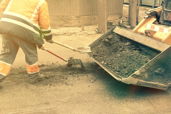 Los trabajadores del camino en uniformes reflectantes naranja brillante utilizan palas para raspar la arena acumulada. mantenimiento de pavimentos de carreteras y carreteras. trabajos de reparación de baches. tonificado — Foto de Stock