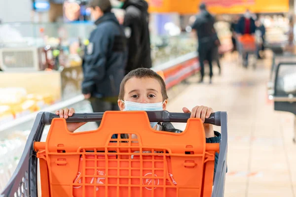 Ребенок в хирургической маске покупает фрукты в супермаркете во время пандемии коронавируса. Мальчик в супермаркете носит медицинскую маску. Карантин коронавируса. тонированные — стоковое фото
