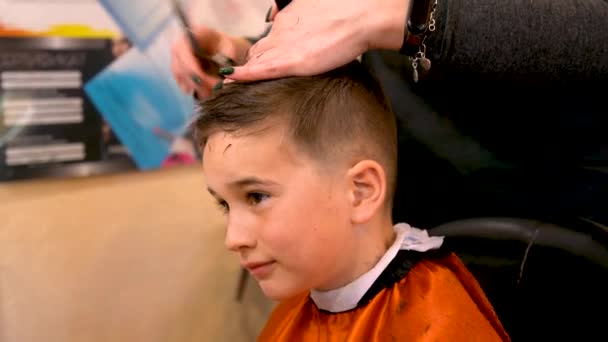 Pojken i frisersalongen. Närbild av tonårspojken som trimmas med professionell elektrisk clipper maskin i frisör, Tonårspojke besöker frisör i frisör butik — Stockvideo