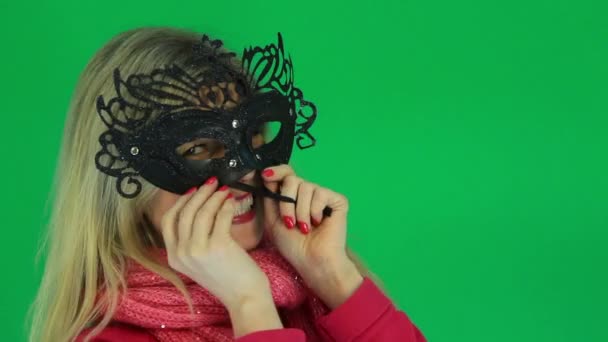 Woman having fun measures the carnival venetian mask on the green background — Stock Video
