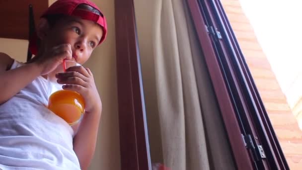 Мальчик пьет сок из стекла через соломинку — стоковое видео