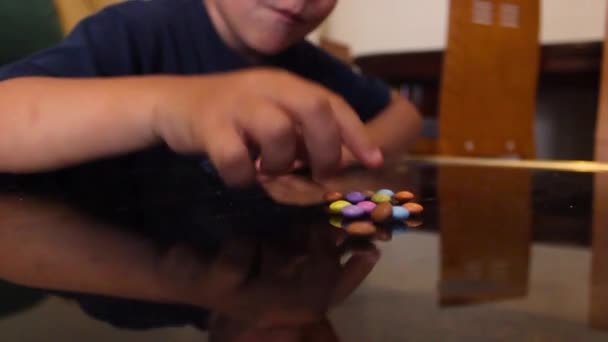 Маленький мальчик собирает конфеты со стола, и один ест их . — стоковое видео