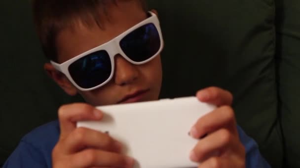 Niño jugando juego en el teléfono móvil con gafas de sol — Vídeos de Stock