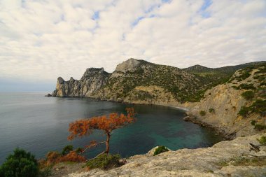 Kasım sabahı, deniz kıyısında, dağlarla çevrili sıcacık bir koyda kayaların manzarası.