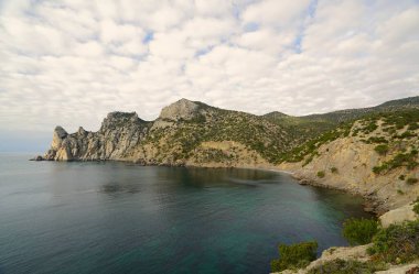 Kasım sabahı, deniz kıyısında, dağlarla çevrili sıcacık bir koyda kayaların manzarası.