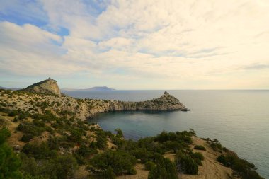Kasım sabahı, deniz kıyısında, dağlarla çevrili sıcacık bir koyda kayaların manzarası.