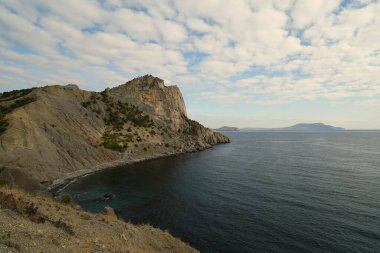 Kasım sabahı, deniz kıyısında, dağlarla çevrili sıcacık bir koyda kayaların manzarası.