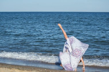 Genç ritmik jimnastikçi deniz kıyısında güzel bir elbiseyle