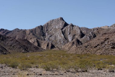 Layered rock formations and dry vegetation in a remote desert mountain landscape