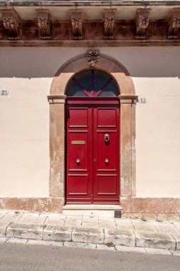 Kemerli kirişli parlak kırmızı giriş kapısı ve güneşli duvarda taş çerçeve.