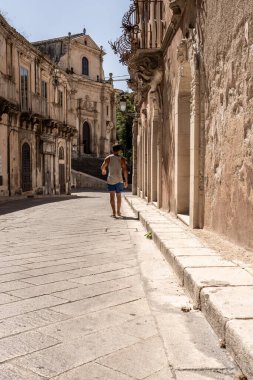 Sicilya 'da barok binaları olan sakin eski kasaba caddesinde yürüyen bir adamın arka görüntüsü
