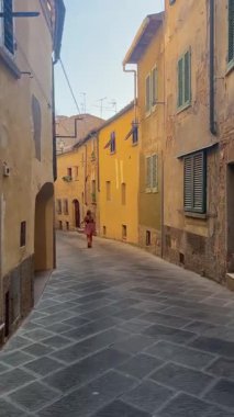 Yalnız kadın figürü, eski taş binalarla kaplı sessiz bir Avrupa şeridi boyunca ilerliyor.