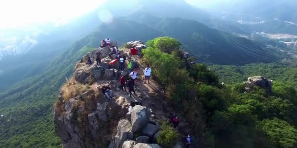 Jóvenes excursionistas en la cima de una montaña sentados en el empinado acantilado disfrutando de la vista del valle — Vídeos de Stock