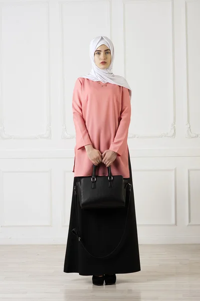 Στούντιο φωτογραφία κορίτσι με ανατολική εμφάνιση, σε μουσουλμανική ρούχα με ένα μαντήλι στο κεφάλι της και την τσάντα στο χέρι, σε ανοιχτόχρωμη επιφάνεια κλασική — Φωτογραφία Αρχείου