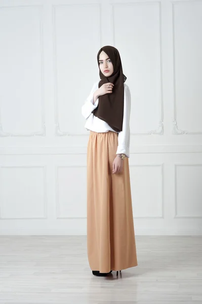 Junge Frau mittleren orientalischen Aussehens in moderner muslimischer Kleidung und schwarzem Schal, einem leichten klassischen Hintergrund — Stockfoto