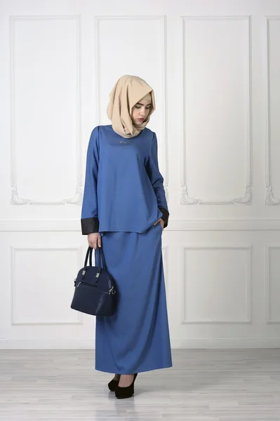 Studiofoto einer jungen Frau europäischen Aussehens in schöner blauer muslimischer Kleidung, eine Tasche in der Hand und ein Taschentuch auf dem Kopf, der klassische helle Hintergrund — Stockfoto