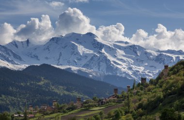 , manzara Svan gözetleme kuleleri ve arka planda karla kaplı dağ zirveleri ve bulutlar, tarım alanları ile Svaneti 