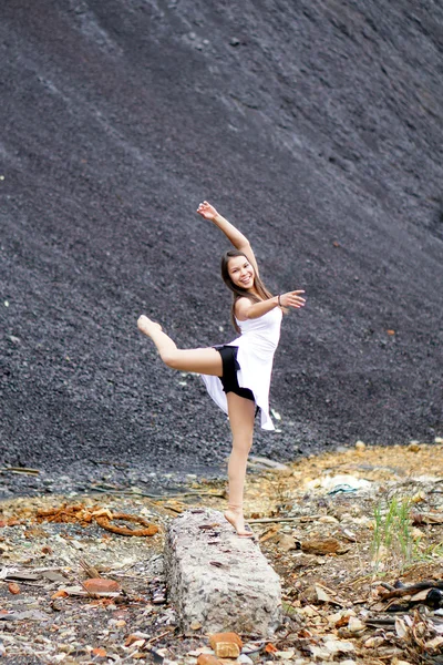 beautiful girl in the gymnastic pose with a smile on his face performs an exercise on landfill