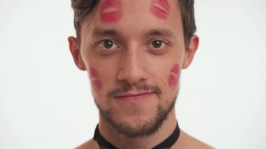 Yüzünde kahverengi sakallı ve bıyıklı kırmızı öpme izleri olan beyaz esmer bir adamın yakın plan portresi. Kameraya bak, flört et, göz kırp, beyaz arka planda izole edilmiş. Kadın Günü konsepti.