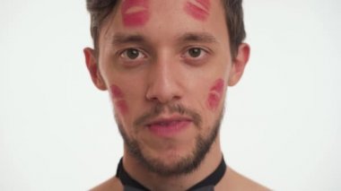 Beyaz, genç, güzel, kırmızı ruj izi olan esmer bir adamın portresi. Siyah papyon takıyor, kameraya bakıyor, beyaz arka planda izole edilmiş bir şekilde konuşuyor. Kadın Günü konsepti