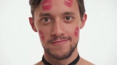 Sakallı ve bıyıklı, ruj izleriyle kaplı yakışıklı, beyaz tenli esmer bir adamın portresini yakından çek. Genç insan gülümser, flört eder, göz kırpar, beyaz arka planda soyutlanır. Romantik konsept.