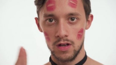 Kahverengi saçlı, gömleksiz, siyah papyonlu, alnında kırmızı ruj lekesi olan genç, neşeli sakalsız bir adamın yakın portresi. Beyaz duvar arkasında izole edilmiş bir erkek öpüşmesi. Kadınlar Günü