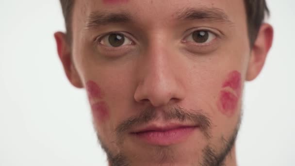 一个漂亮的白种人黑发男人 脸上有红色口红的吻印 用手和嘴表现出口交的姿势 情人男孩在白色背景上制造禁物标志 近景肖像 — 图库视频影像