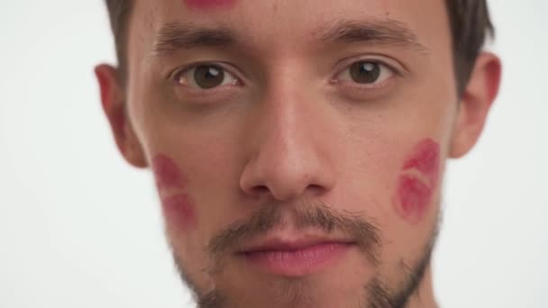 赤い口紅のキスをした1人のハンサムなヨーロッパ人の肖像画は オーラルセックスのジェスチャーを閉じるを示す顔に刻印されています 男性は白の背景に禁止されたセックスシンボル 驚きを作る 不貞概念 — ストック動画