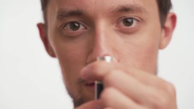 Young stupid 20s brunette bearded man cross-eyed focus on pink girls lipstick in hands. Guy is fooling, playing with lady accessories isolated on white background close up. Portrait of dumb person.
