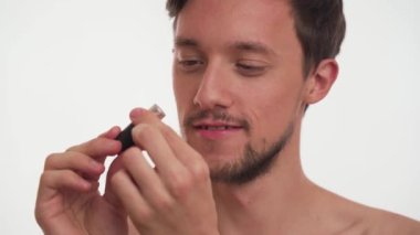 Zeki, yarı çıplak, esmer, sakallı, aptal, kadınlara bakan, pembe rujlu, beyaz arka planda izole edilmiş elleri tutan adam. Genç bir adam ilk kez makyaj yapmaya hazır değil..