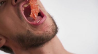 Genç, beyaz sakallı, ağzı açık, lezzetli balıklar koyan, zevkle yiyen, arka planda izole edilmiş yavaş çekimde çiğneyen beyaz sakallı adam. Lezzetli sağlıklı yiyecekleri seven bir adamın portresi.