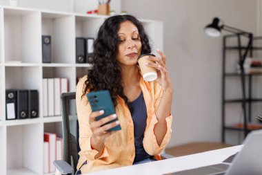 Cep telefonu kullanan ve kahve içen bir kadın..