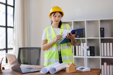 İnşaat alanında çalışan Asyalı kadın mühendis ya da kadın mimar ya da beyaz kasklı işçi. Dizüstü bilgisayar ve plan kullanan kadın mühendis ya da mühendis.