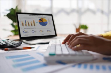 Klavyeye yazı yazan kişinin elleri dizüstü bilgisayardaki finansal verileri grafiklerle analiz ediyor.