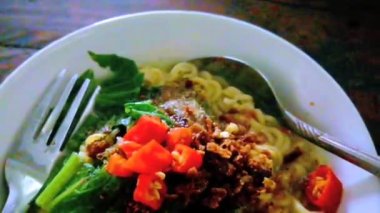 Beyaz kasede servis edilen ve kaşıkla tamamlanmış erişteler baharatlıdır (Mie Instan Kuah), yemek videosu.