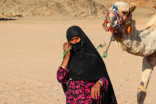 ХУРГАДА, ЭГИПТ - 24 апреля 2015 г.: Старуха-верблюдица из деревни Бедуин в пустыне Сахара со своим верблюдом, Египет, ХУРГАДА, 24 апреля 2015 г.
