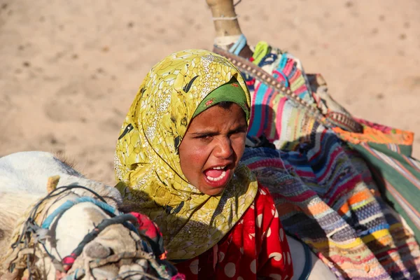 HURGHADA, EGYPT - Apr 24 2015: The young girl-cameleer from Bedouin village in Sahara desert with her camel, shouting inviting tourists, Egypt, HURGHADA on Apr 24, 2015 — Stock Photo, Image