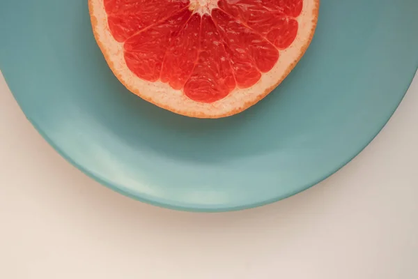 Bir dilim kırmızı greyfurt mavi bir tabakta duruyor.