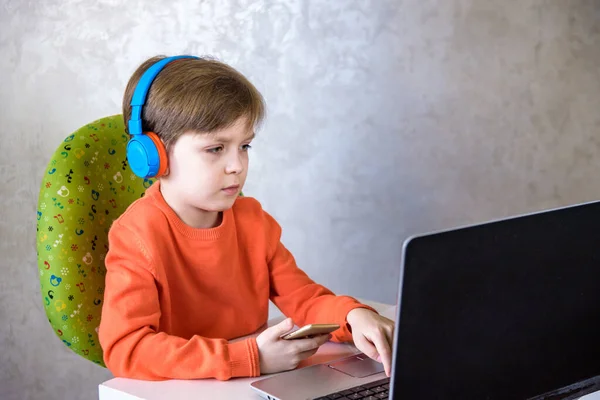 technology, home education and people concept - boy in headphones having classes trough internet on laptop computer at home. Lockdown remote safe communication.