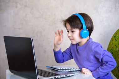 Evde dizüstü bilgisayarla oturup ders çalışırken kameraya bakan yakışıklı bir Avrupalı çocuk. Modern eğitim ve çalışma kavramı.