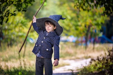Sivri şapkalı çocuk dışarıda sihirli değnekle oynuyor. Küçük büyücü. Cadılar Bayramı konsepti.