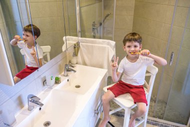 Küçük sevimli bir çocuk diş fırçasıyla dişlerini fırçalıyor. Giyindiği beyaz tişörte bir reklam yazısı yazılabiliyor. Çocuk sağlığı ve ilaç kavramı.