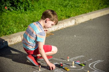Komik çocuk tebeşirle trafik arabası çizerken eğleniyor. Yazın açık havada çocuklar için yaratıcı bir eğlence. Zorlu trafik kuralları kavramı.