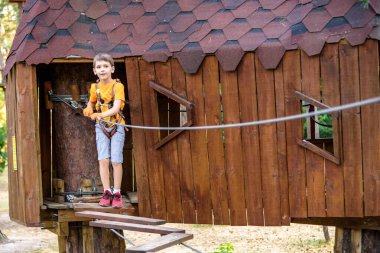 Çocuk bir ağaç eve tırmanıyor. Güvenlik tüfeği, ormanın ve gökyüzünün arka planında bir ipe bağlanır. Açık havada sağlıklı oyunlar.